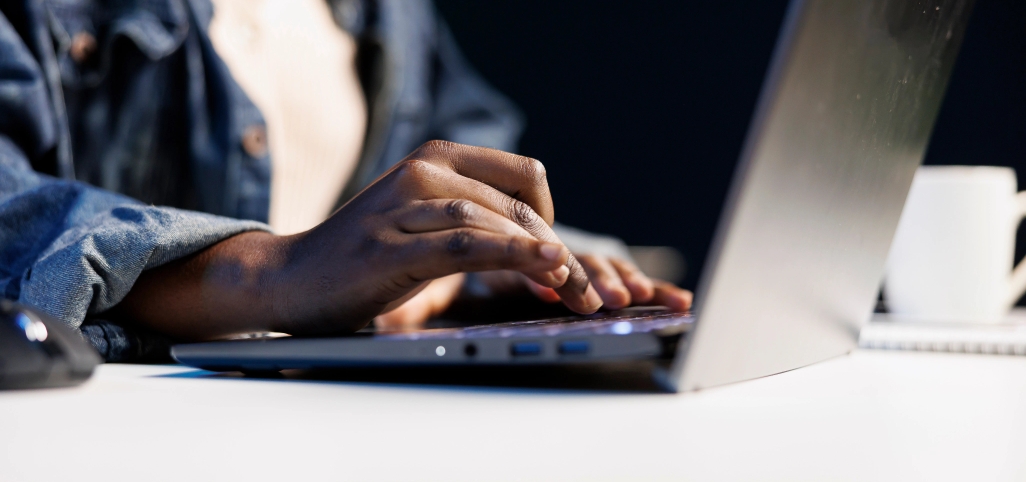 A person in a denim jacket types on a laptop at a desk, with a white cup and notebook visible in the background—perhaps researching an Ohio Discrimination Lawyer.