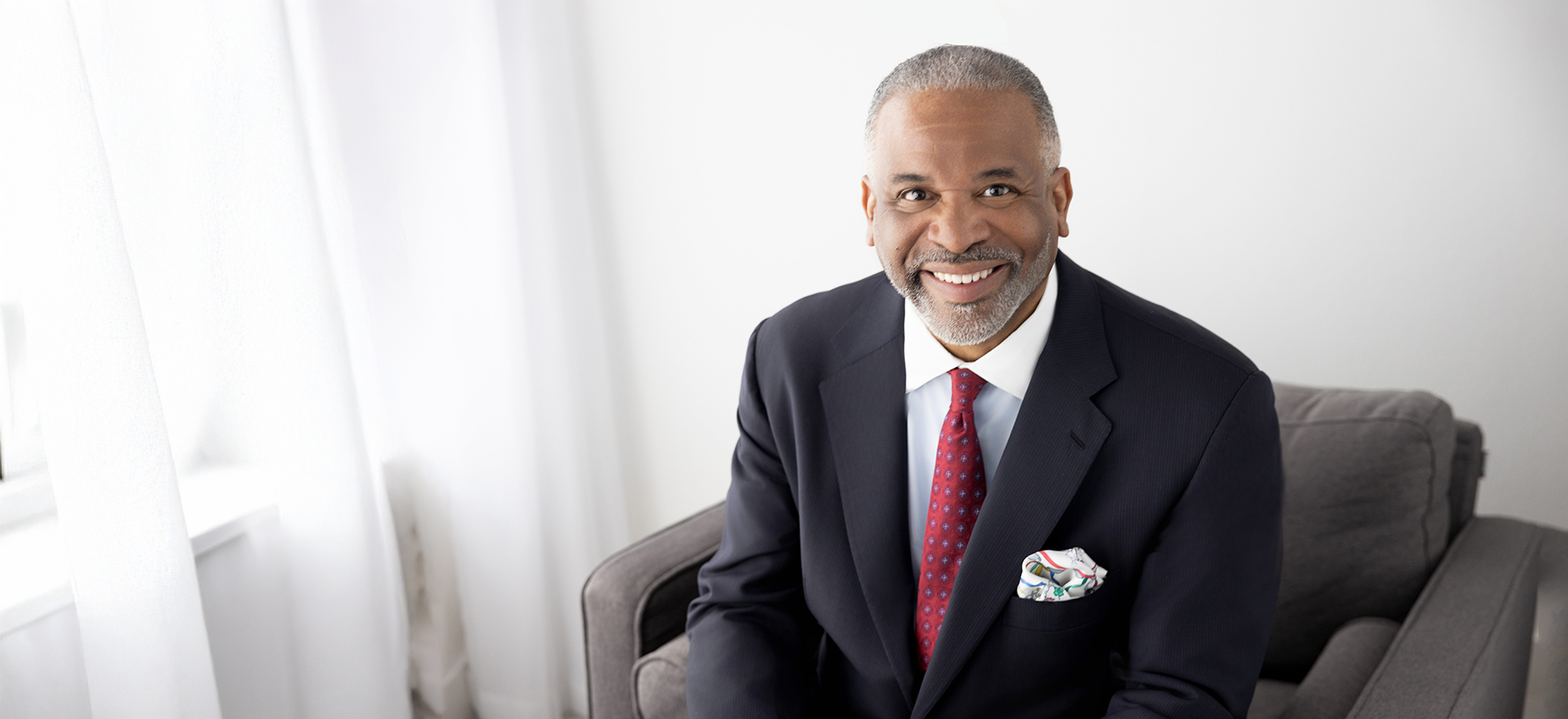 Attorney Gregory J. Vincent seated in chair smiling at camera, wearing dark suit and red tie